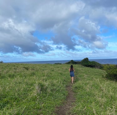 A woman walking away down a cliffside path on a Hawaii ocean cliff