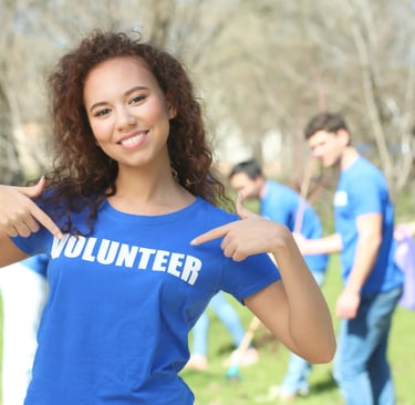 a woman in a blue shirt is pointing at her shirt that states she is a volunteer