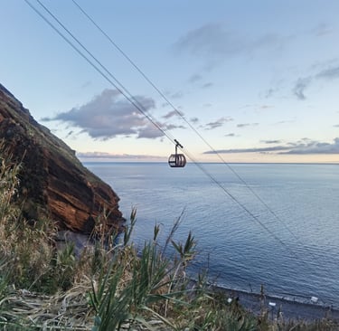 A scenic cable car descending a coastal cliff over the blue Atlantic Ocean in Madeira at sunset.