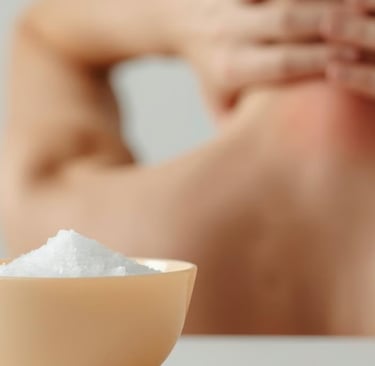 Человек держится за шею, ощущая напряжение или боль. На переднем плане соль, символ расслабления