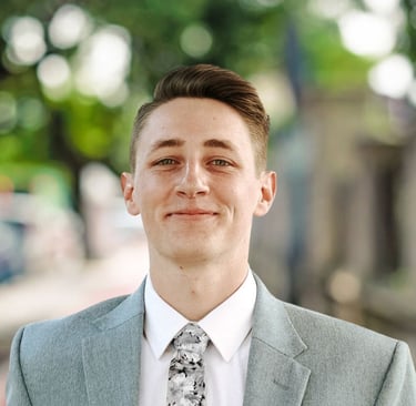 Portrait of Parker Oelrich, smiling slightly while wearing a light gray suit jacket, white shirt, an
