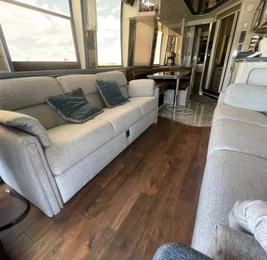Luxury RV interior with grey fabric sofas, dark wood flooring, and a dinette area in a modern motorhome.