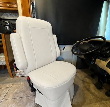 Luxury white leather captain's chair inside a motorhome RV cockpit next to the steering wheel.