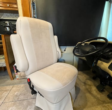 A plush tan leather swiveling captain chair in a luxury RV driver cabin with a black steering wheel.