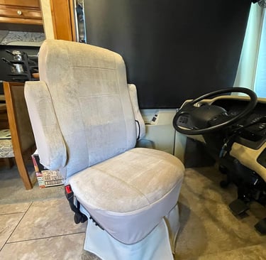 Beige fabric swivel driver's seat inside a motorhome RV cockpit next to the steering wheel.