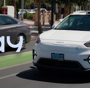 White self-driving electric car with roof-mounted sensor driving on a city street.