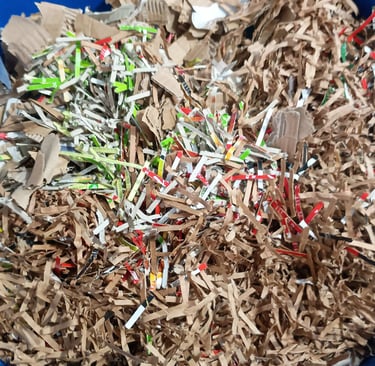 A blue plastic bin filled with shredded brown cardboard and colorful recycled paper strips.