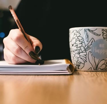 a person writing on a notebook with a cup of coffee