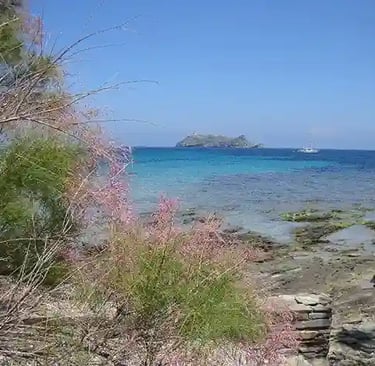 Photo de la mer en Corse d'un bleu intense avec gros rocher au loin et un bateau