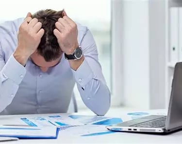 Homme stressé tête baissée avec coudes sur son bureau et ses deux mains sur sa tête