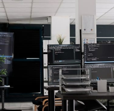 Kantor pengembangan perangkat lunak modern dengan beberapa monitor yang menampilkan kode, melambangkan lingkungan kerja softw