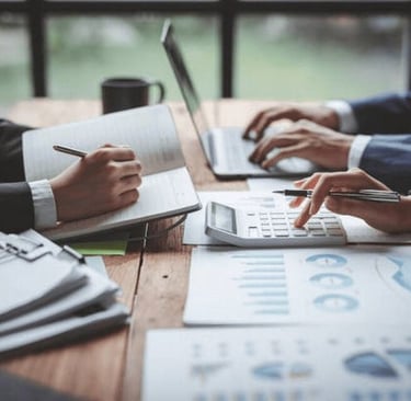 Tim bisnis menganalisis laporan keuangan dan data kinerja menggunakan laptop, catatan, serta grafik untuk mendukung pengambil