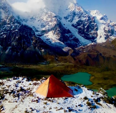 Orange tent at a snowy mountain campsite overlooking a turquoise alpine lake and glaciers in Peru. 