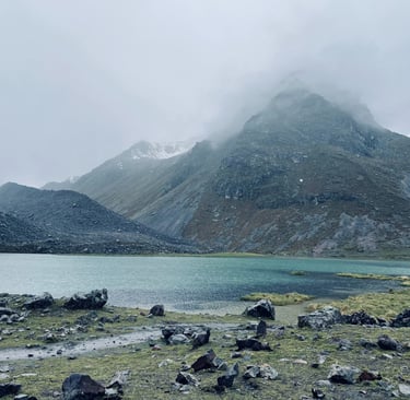 Misty mountain range in Peru overlooking a turquoise glacial lake in a rocky alpine landscape.