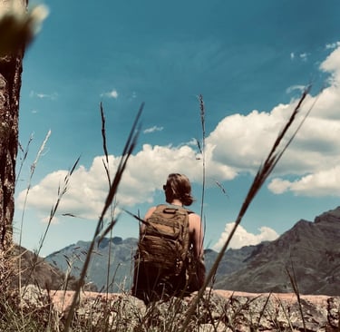 A hiker with a backpack sitting on a stone wall overlooking scenic mountain under a blue sky in Peru