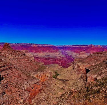 Panoramic view of the Grand Canyon National Park with red rock layers under a clear blue sky.