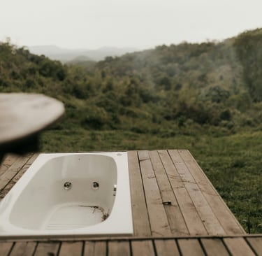A modern outdoor bathtub built into a wooden deck overlooking a lush green valley and mountains.
