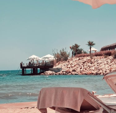 Luxury beach resort with sun loungers, turquoise ocean water, and a wooden pier under a blue sky.