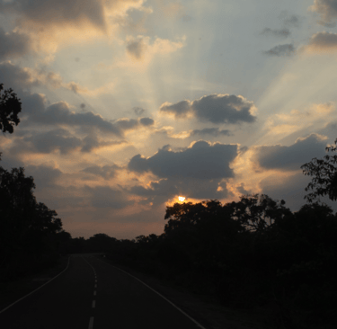 Golden sun rays breaking through clouds over a scenic asphalt highway at sunset.
