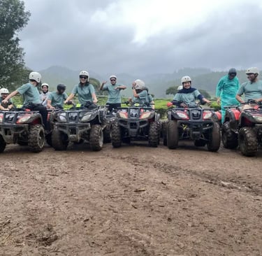 Sekelompok orang dewasa mengendarai ATV di jalur tanah berlumpur di tengah perkebunan teh yang luas.