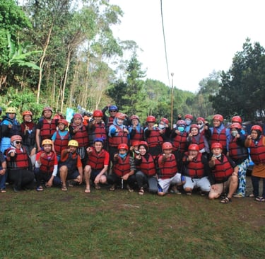 Peserta team building perusahaan sedang berpose mengenakan helm dan jaket pelampung sebelum kegiatan rafting di Bandung.