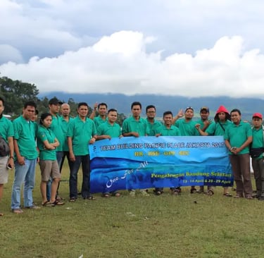Sekelompok karyawan yang mengenakan kaus hijau kompak berpose di samping spanduk bertuliskan "TEAM BUILDING PACIFIC PLACE JAK
