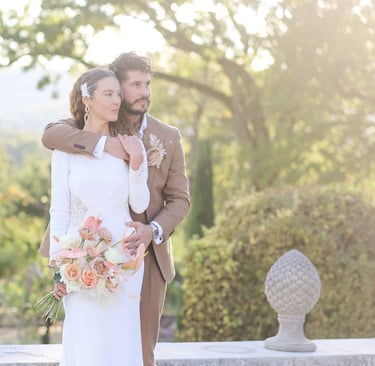 Elegant bride in a long-sleeve wedding dress and birdcage veil posing with the groom in a tan suit at a garden wedding.