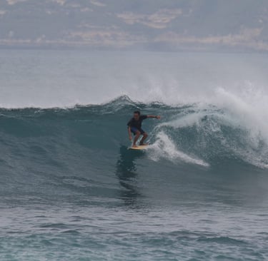 Romi riding a wave while surfing at Ekas beach, showcasing his skills as an experienced instructor.