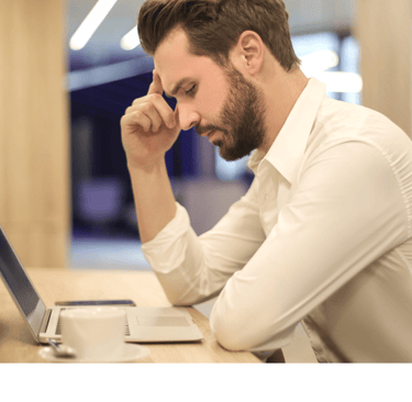 A man sitting thinking at a desk with a laptop computer