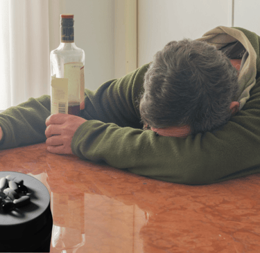 A man sitting at a table with a bottle of alcohol