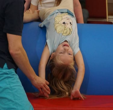 a young girl is upside down in a SEND gymnastics session with coach support