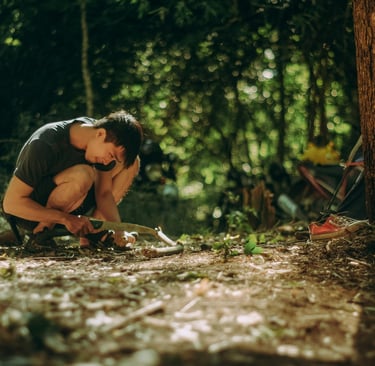 Person using firestarter in forest clearing, learning essential fire building survival skills