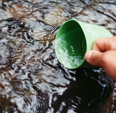 Metal cup collecting river water, representing hydration and water purification outdoors