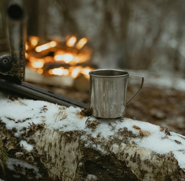 Metal mug and stick by snowy campfire, demonstrating off-grid outdoor cooking
