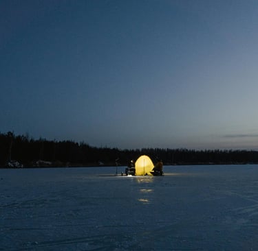 Ice fishing tent glowing on frozen lake at dusk, cold weather survival and winter sheltering