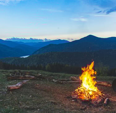 Campfire burning on mountain ridge at sunset, survival warmth, outdoor cooking, and wilderness shelter