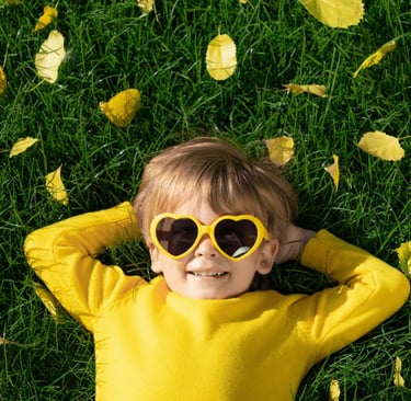 Lachendes Kind mit Sonnenbrille auf Wiese – Selbstvertrauen & Leichtigkeit durch Hypnose für Kinder