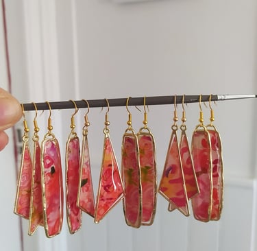 a person holding a string of earrings with red and yellow flowers