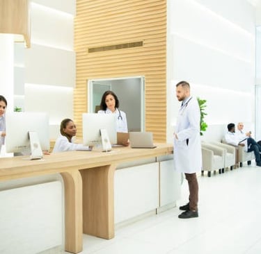 Recepción del consultorio médico con tres asistentes y un médico.