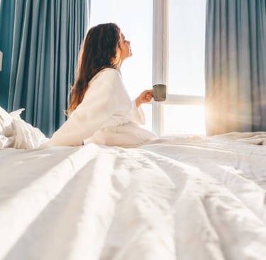 Mujer tomando café en la cama frente a la ventana