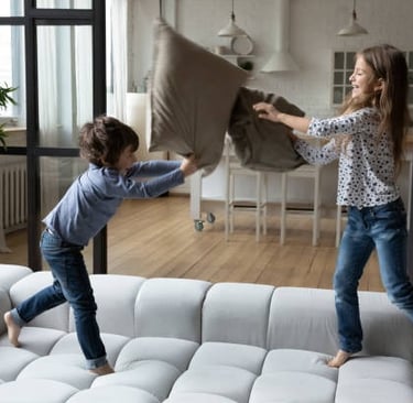 Dos niños teniendo una pelea de almohadas en el sofá