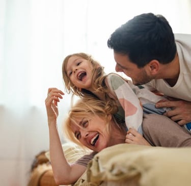 Una familia feliz riendo, madre, padre y una niña entre ellos.