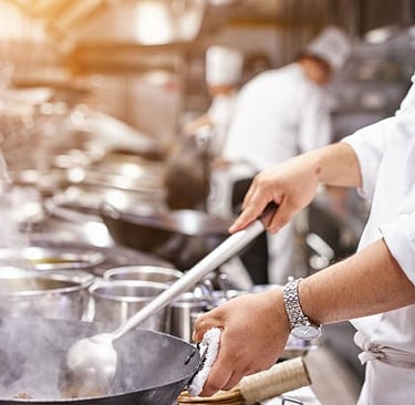 El chef revuelve la comida en una sartén.Lleva un reloj en la muñeca izquierda.