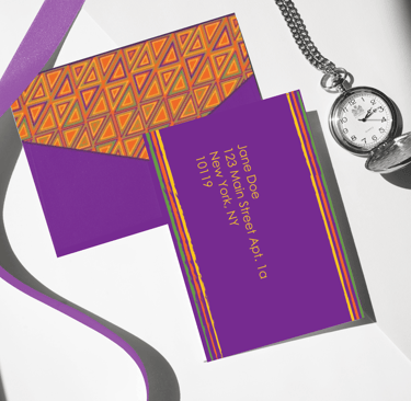 Purple custom envelope with geometric patterns next to a silver pocket watch and silk ribbon.