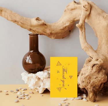 Yellow thank you card with geometric designs on a rustic display with driftwood and a brown glass vase.