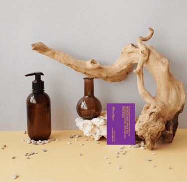 Amber glass apothecary bottles and driftwood aesthetic spa branding flat lay with purple card.