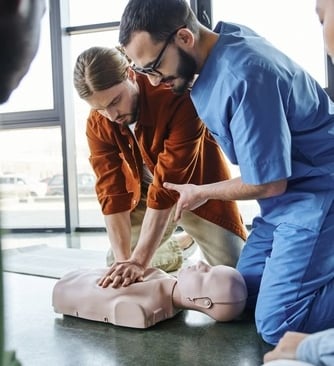 A male nurse teaching a man to administer first aid CPR on a dummy