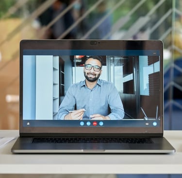 A laptop screen showing a video call with a man in a business shirt holding a pen