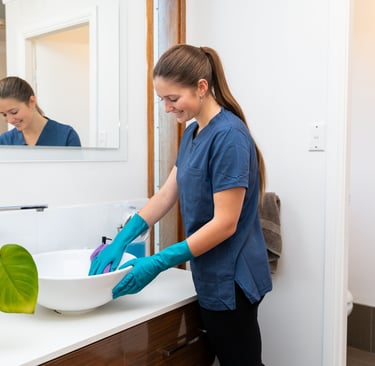 a woman in a blue shirt and gloves cleaning a sink