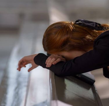 Individual resting head on crossed arms in a church pew, beside a book, in quiet reflection.